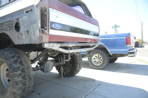 1979 Ford Bronco - Two Ford trucks are parked side-by-side on a sunny day, one with a custom bumper and exposed metal.