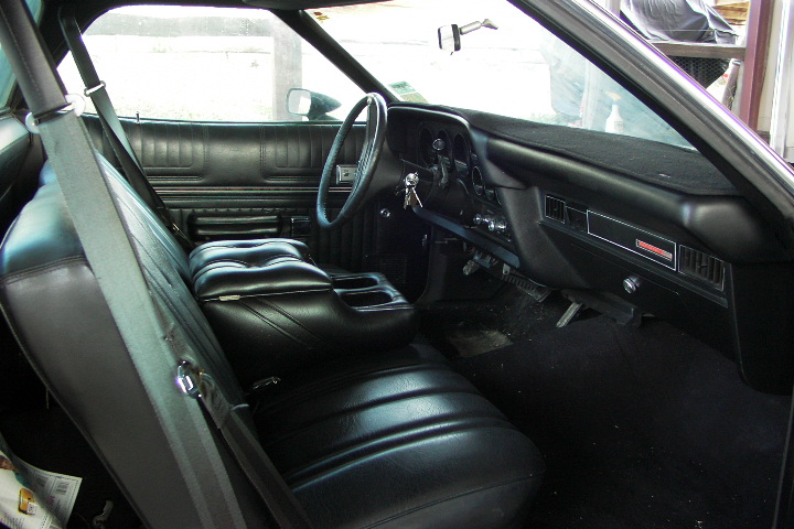 Black bench-seat interior of vintage coupe with dashboard and gauges