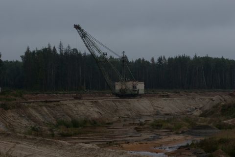 1987 Ford Bronco - A large dragline excavator operates in a quarry under an overcast sky, with a dense forest bordering the site.