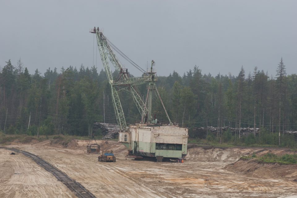 Dragline excavator and bulldozer in a quarry with a forest background
