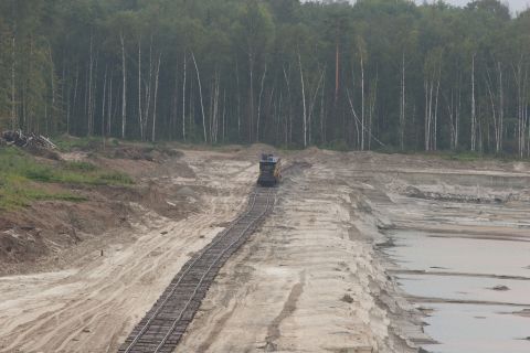 1987 Ford Bronco - A train travels on tracks through a quarry, with a dense forest bordering the landscape.
