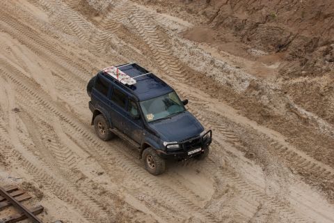 1987 Ford Bronco - A dark blue SUV navigates a sandy terrain, leaving tire tracks behind.