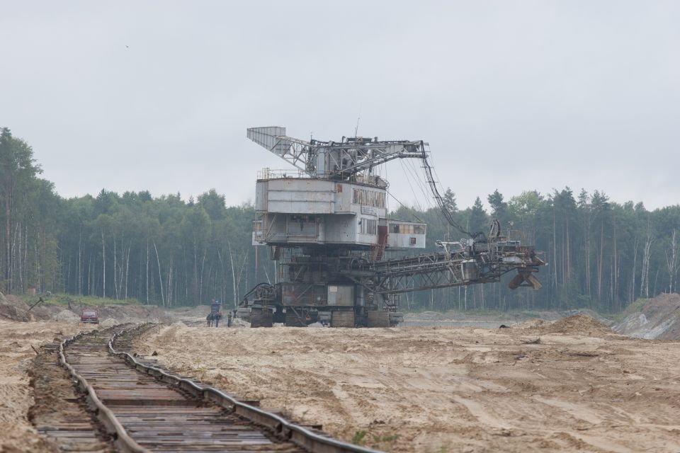 Giant excavator in a sandy area with trees in the background and train tracks in the foreground