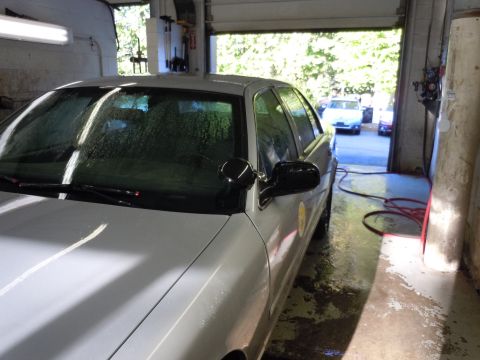 2001 Ford Crown Victoria - A white sedan is parked inside a garage with the door open, revealing another vehicle outside.