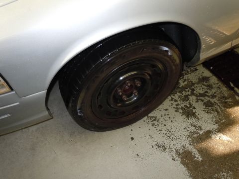 2001 Ford Crown Victoria - Close-up of a silver car's front wheel and fender area, with a black steel rim.