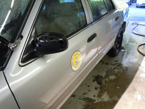 2001 Ford Crown Victoria - A silver sedan, possibly a police vehicle, is parked on a wet surface with a missing side mirror.