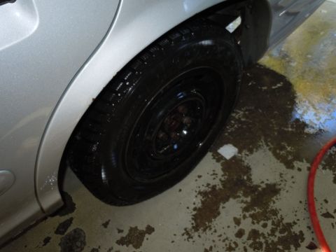 2001 Ford Crown Victoria - Close-up of a silver car's rear wheel and fender, with a wet floor visible.
