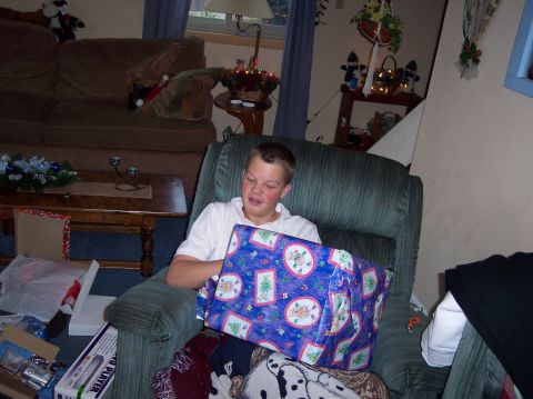 1990 Ford Bronco - A boy sits in a recliner, eagerly opening a large, brightly wrapped gift. The scene is set indoors, likely during the holiday season.
