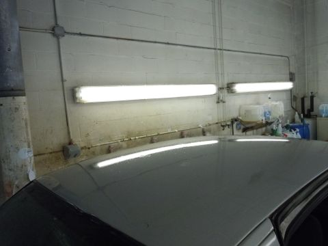 2001 Ford Crown Victoria - The top of a gray car is visible, reflecting the bright fluorescent lights of what appears to be a workshop or garage.