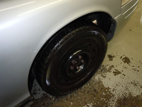 2001 Ford Crown Victoria - Close-up of a silver car's front fender and wheel, showing a black steel rim and tire.
