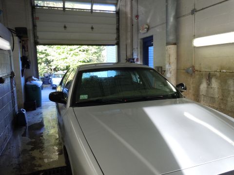 2001 Ford Crown Victoria - A white sedan is parked inside a garage, with another vehicle visible through the open garage door.