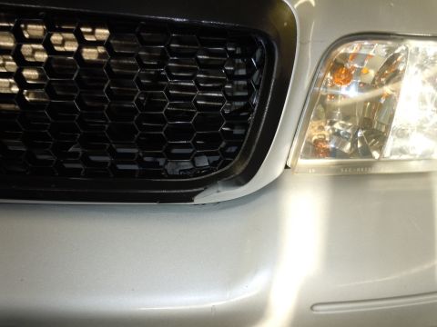 2001 Ford Crown Victoria - Close-up of a silver car's front end, showing a black honeycomb grille and a headlight assembly.