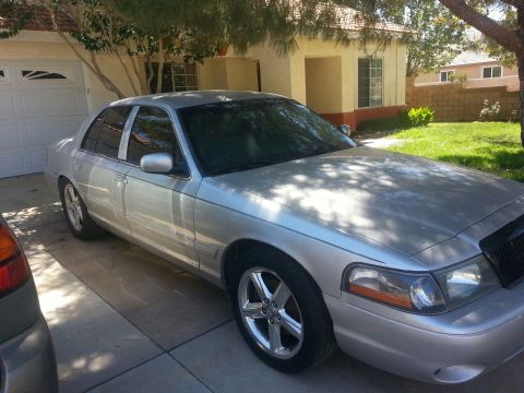 1998 Ford Crown Victoria - A silver sedan is parked in front of a house and garage on a sunny day.
