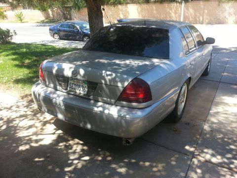 1998 Ford Crown Victoria - A silver sedan is parked on a concrete driveway, with another car visible in the background.
