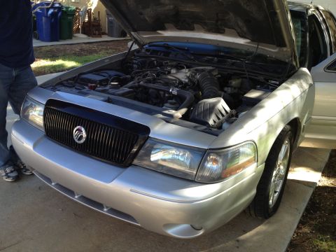 1998 Ford Crown Victoria - The front of a silver Mercury Grand Marquis is shown with the hood up, revealing the engine compartment.