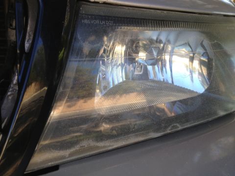 1998 Ford Crown Victoria - The headlight assembly shows some wear and dirt, with regulatory text imprinted on the lens.