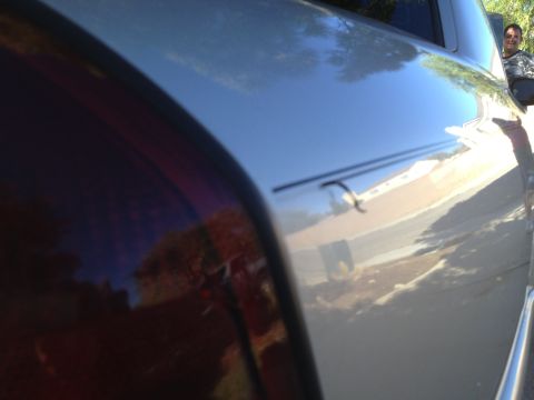 1998 Ford Crown Victoria - A person is reflected in the shiny paint of a car's rear quarter panel, near the taillight.