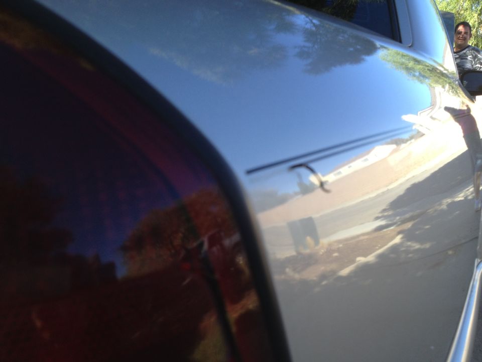 Low-angle reflective view along a silver car's roofline with a person reflected