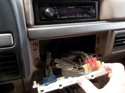 1995 Ford Bronco - A hand removes a panel from a car's dashboard, revealing wiring and a Kenwood stereo above.