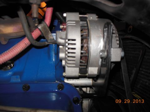 1979 Ford F-150 - Close-up view of an alternator installed on a blue engine block, with visible hoses and wiring.
