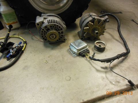 1979 Ford F-150 - Two alternators and a voltage regulator are laid out on a concrete floor, possibly for a vehicle repair or upgrade.