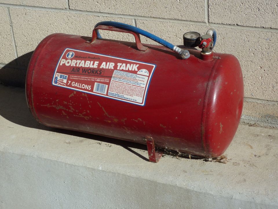 Red portable air tank with gauge and hose, labeled "AIR WORKS 7 GALLONS"