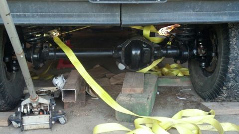 1996 Ford F-150 - Underbody view of a vehicle's rear axle and suspension system, held in place with yellow straps and supported by a jack and blocks.