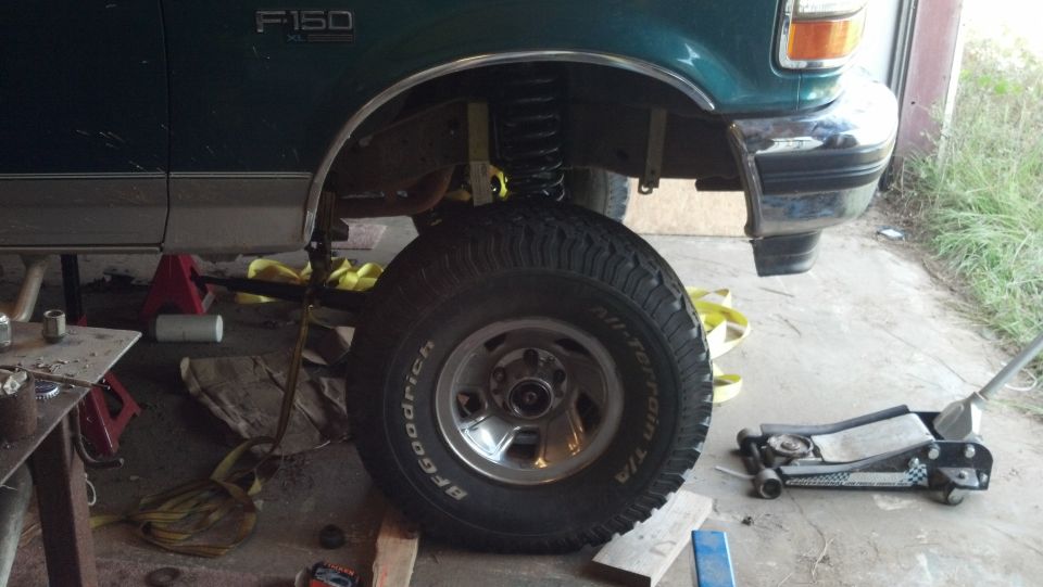 Green 1996 Ford F-150 side view, front fender and wheel visible, lifted with jack stands