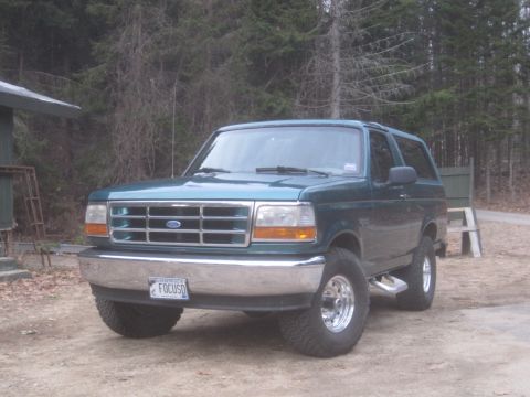1996 Ford Bronco - Green 1996 Ford Bronco parked in a dirt lot with trees behind it. License plate is visible.