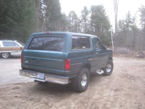 1996 Ford Bronco - Rear three-quarter view of a green Ford Bronco SUV, with another vehicle in the background.