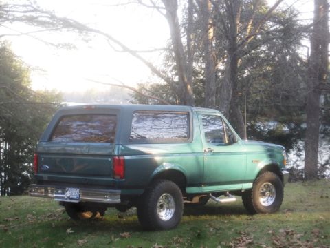 1996 Ford Bronco - A green Ford Bronco is parked on a grassy area next to trees with a body of water in the background.