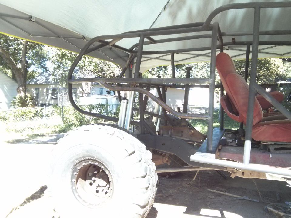 Custom off-road vehicle frame with red seats and large tire, side view