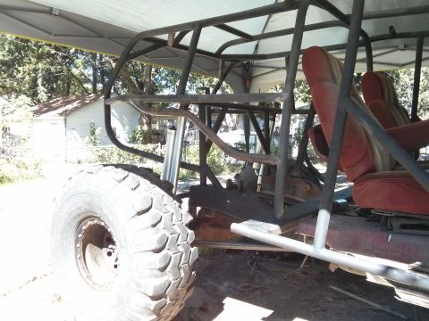 1986 Ford Bronco - Custom buggy frame with red seats and large off-road tire, parked under a canopy.