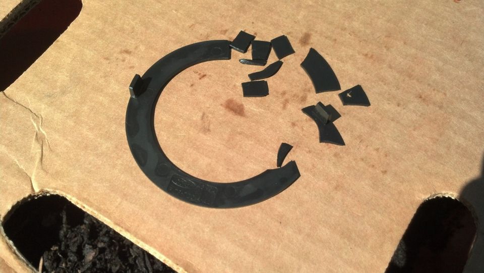 Broken black plastic Ford trim ring with fragments arranged on cardboard