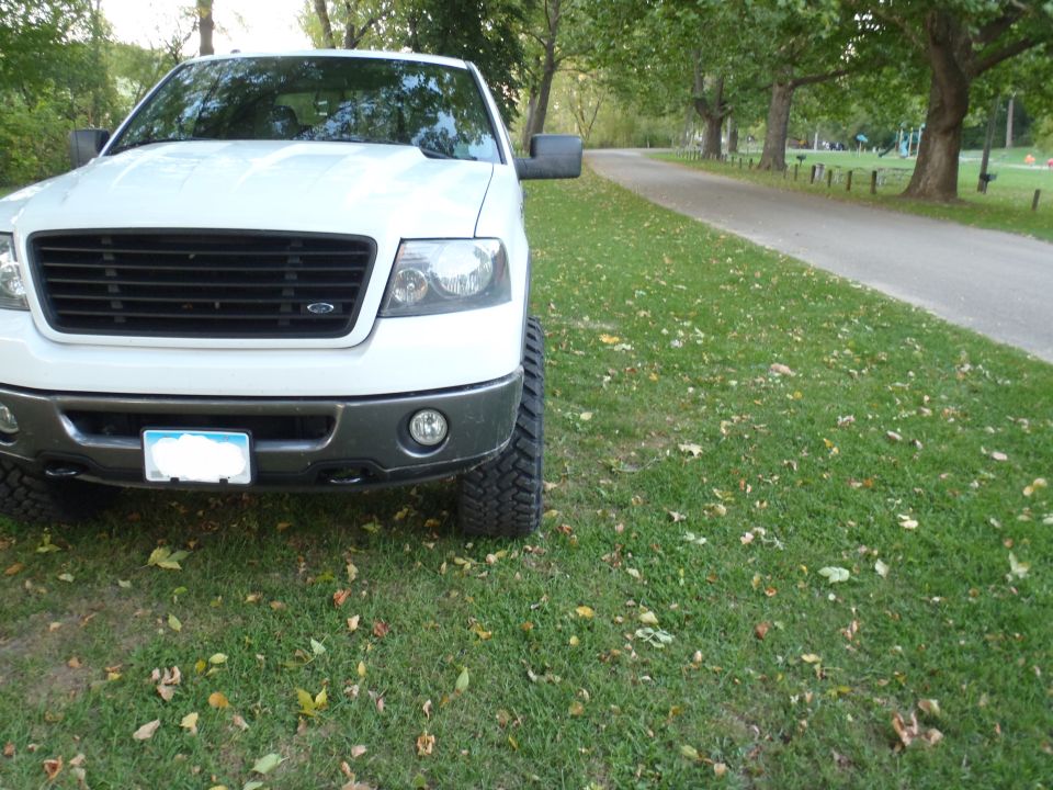 White Ford F-150 truck, front view, parked on grass next to a road