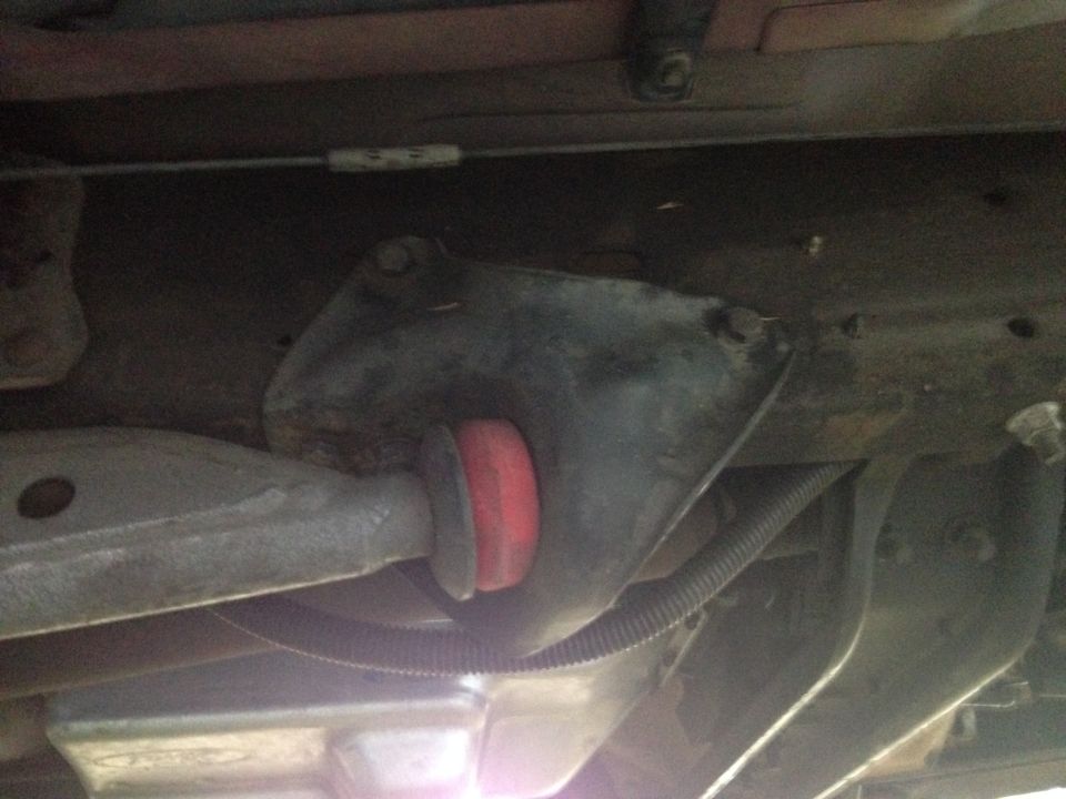 Underside view of a suspension radius arm with a red bushing and black protective conduit