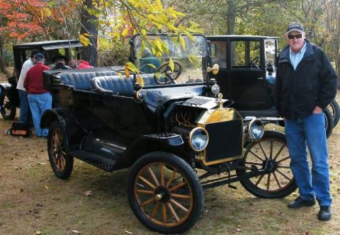 1915 Ford Model T - A man poses with a classic black Ford Model T touring car, with another similar vehicle in the background.