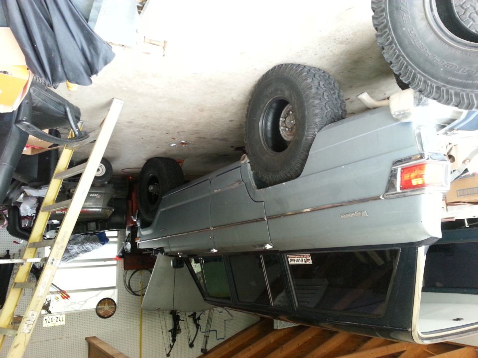 Gray Jeep Wagoneer with aftermarket wheels and tires, seen from the side in a garage