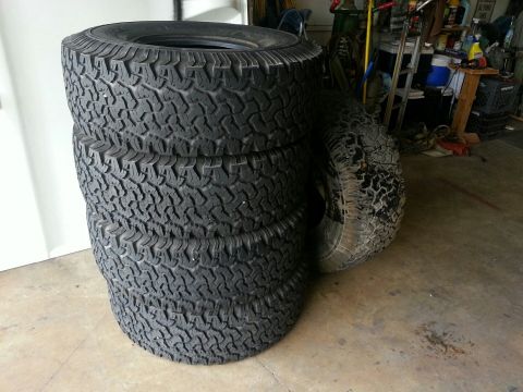 1982 Jeep Wagoneer - A stack of four off-road tires sits on a garage floor next to another tire.