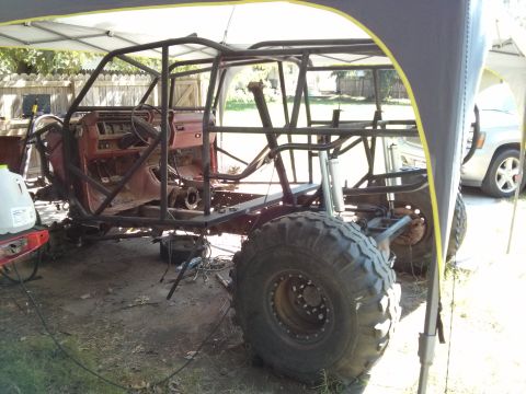 1986 Ford Bronco - Modified vehicle chassis with a prominent roll cage and large off-road tires, partially covered by a canopy.