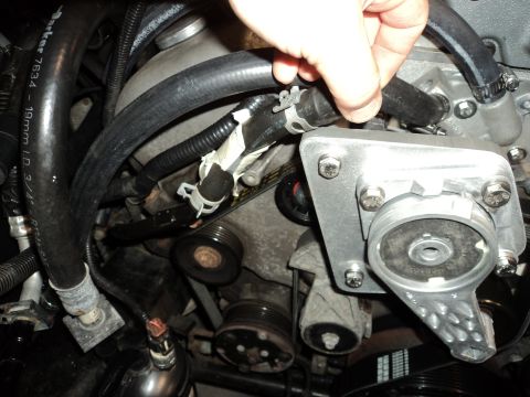 2004 Mercury Grand Marquis - Close-up of a hand adjusting a hose connected to a supercharger bracket in an engine bay.