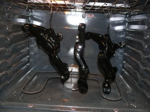 Three black car parts hanging in an oven, likely being painted