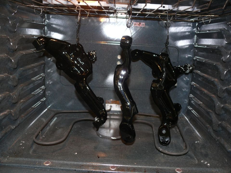Three black car parts hanging in an oven, likely being painted