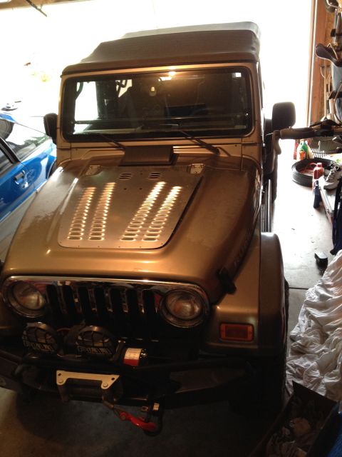 2005 Jeep Wrangler - A gold Jeep Wrangler is parked in a garage, showing its front grille and hood details.