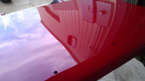 1972 Pontiac Trans Am - A red car hood reflects a building and sky, with visible holes on its surface.