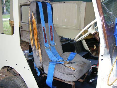 Interior view of a vehicle with torn seats and blue racing harnesses with "PYROTECT" text