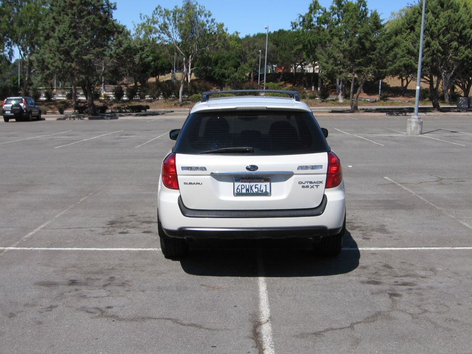 Rear view of a white Subaru Outback parked in a lot. Another SUV is parked in the distance