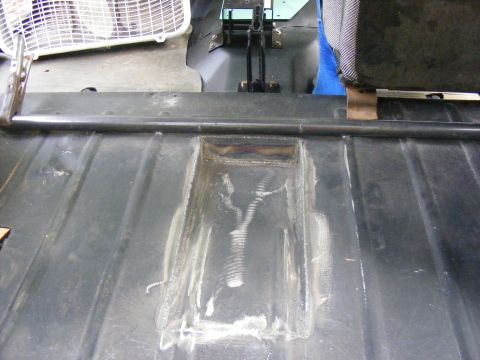 Welded repair on a vehicle's metal floor pan, with a seat and fan visible