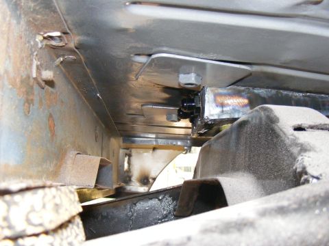 Close-up of vehicle frame with bolted metal plates and suspension parts. Some rust visible