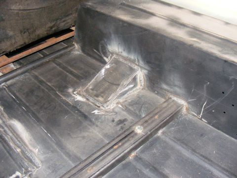 Close-up of a vehicle's metal floor pan with visible welds and repair work